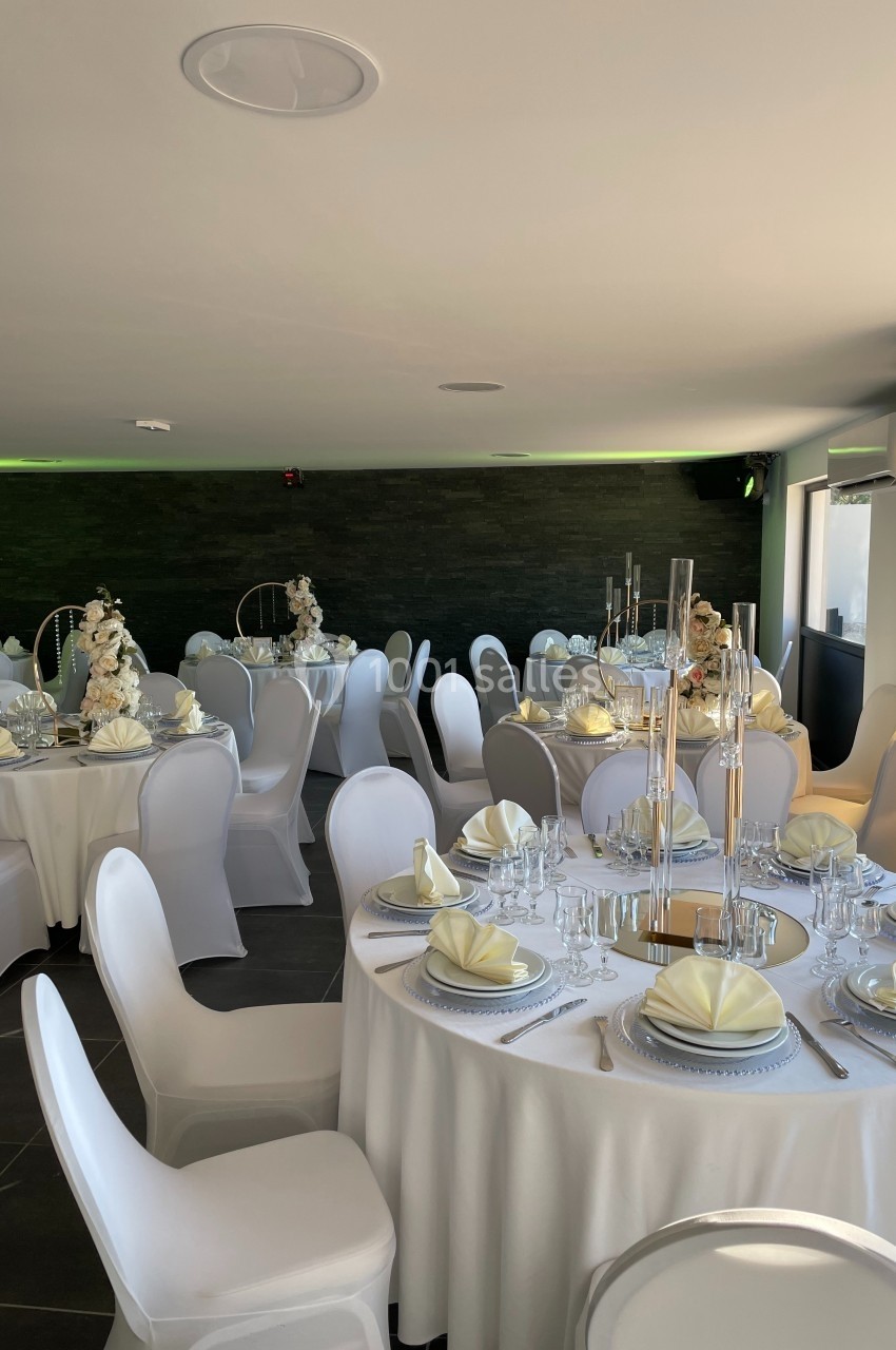 Salle de réception élégamment décorée avec des tables rondes, nappes blanches, serviettes pliées et centres de table…