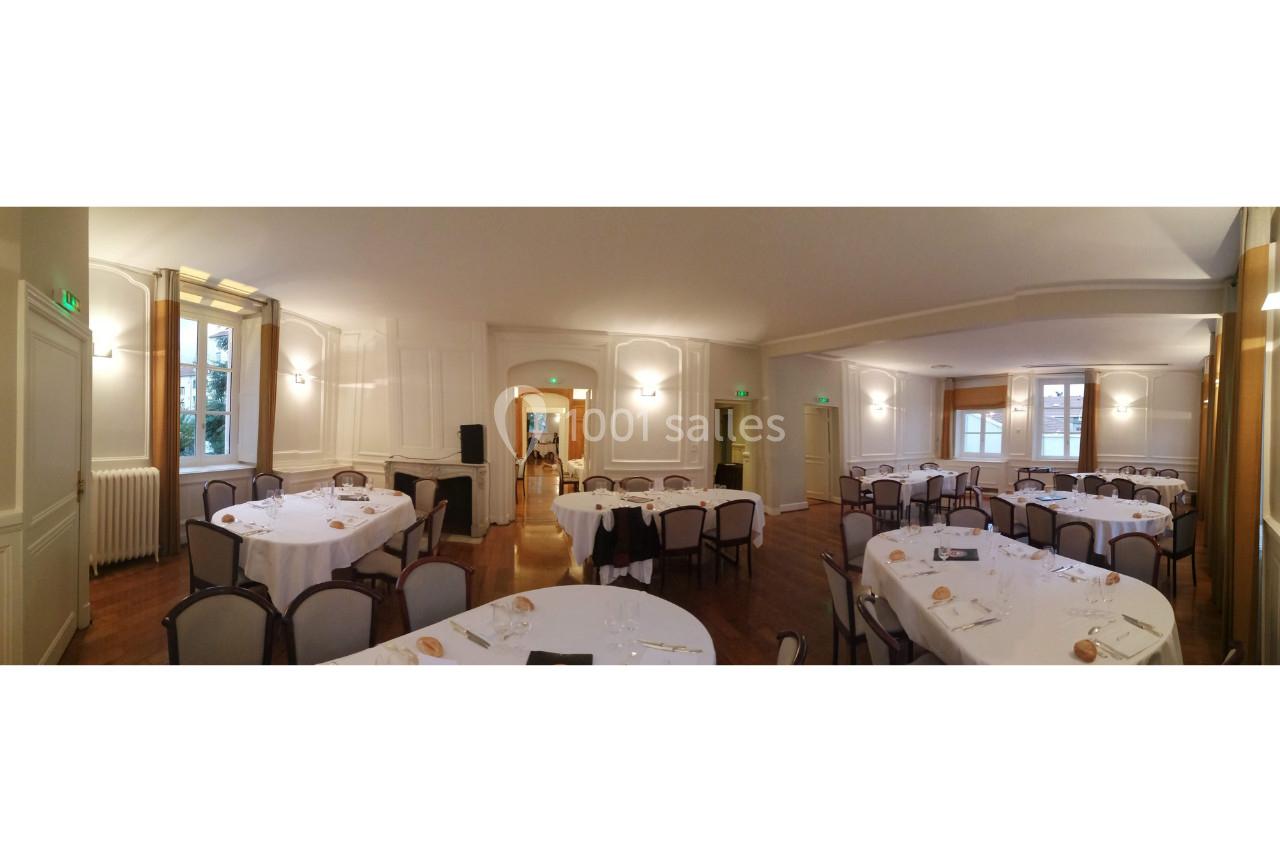 Salle de réception lumineuse avec tables rondes dressées pour un repas, chaises alignées et décor sobre.