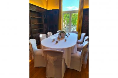 Salle élégante avec tables rondes et chaises blanches, décorée de bouquets, éclairée par des luminaires modernes.