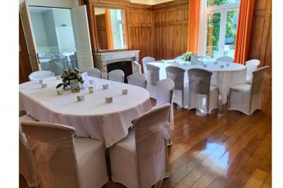 Salle élégante avec tables rondes et chaises blanches, décorée de bouquets, éclairée par des luminaires modernes.