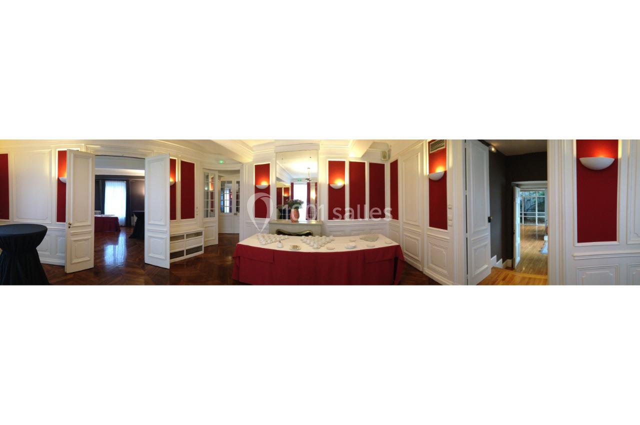 Salle élégante avec murs rouges et blancs, table drapée de rouge au centre, éclairage doux et parquet en bois.