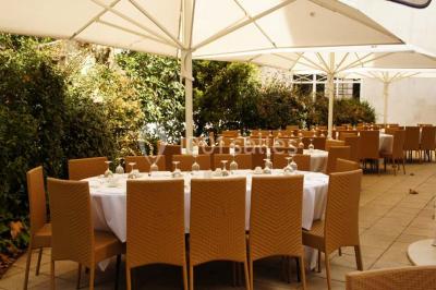 Salle élégante avec tables rondes et chaises blanches, décorée de bouquets, éclairée par des luminaires modernes.
