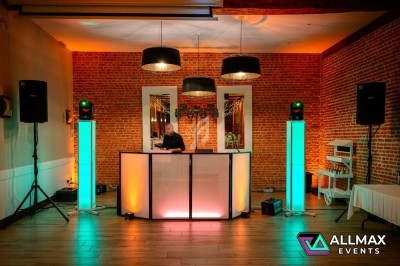 Poste de DJ éclairé avec des lumières colorées dans une salle au mur de briques, équipé de haut-parleurs et de décorations.