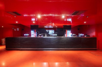 Hall d'entrée avec murs aux formes ondulées, sol à motifs géométriques et escalier menant à une porte noire.