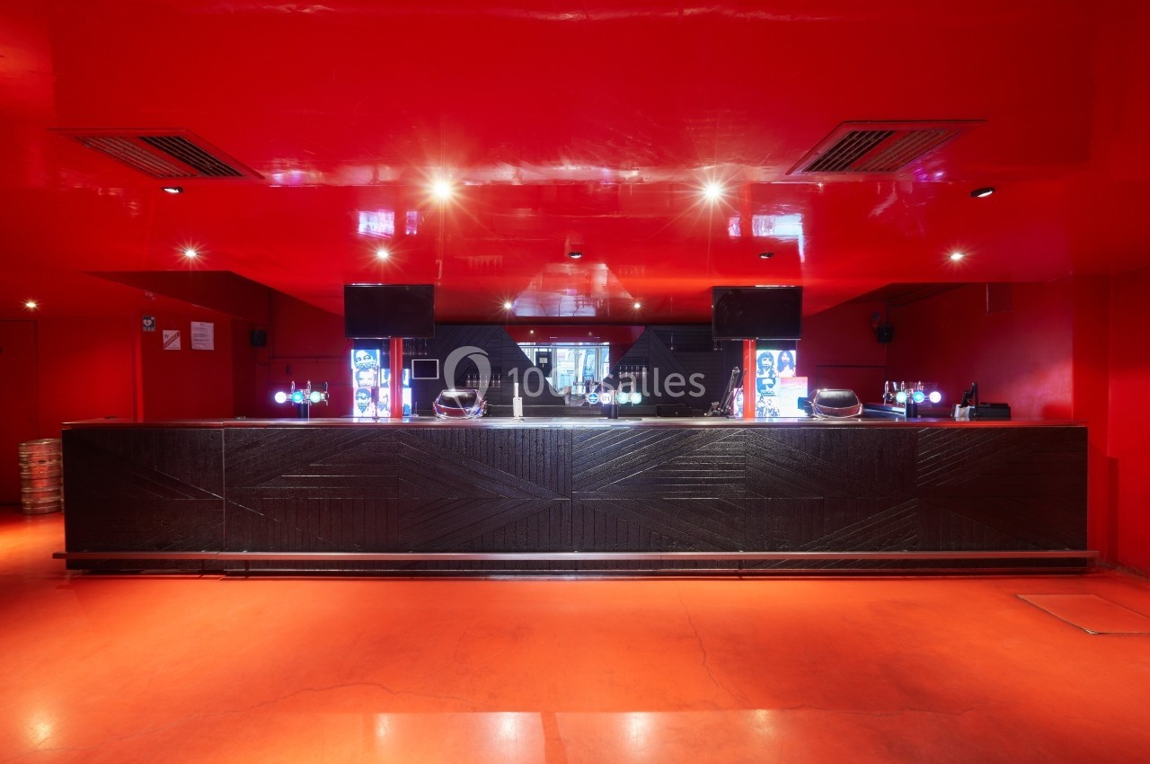 Comptoir de bar moderne en bois sombre dans une pièce aux murs et plafond rouges avec éclairage tamisé.