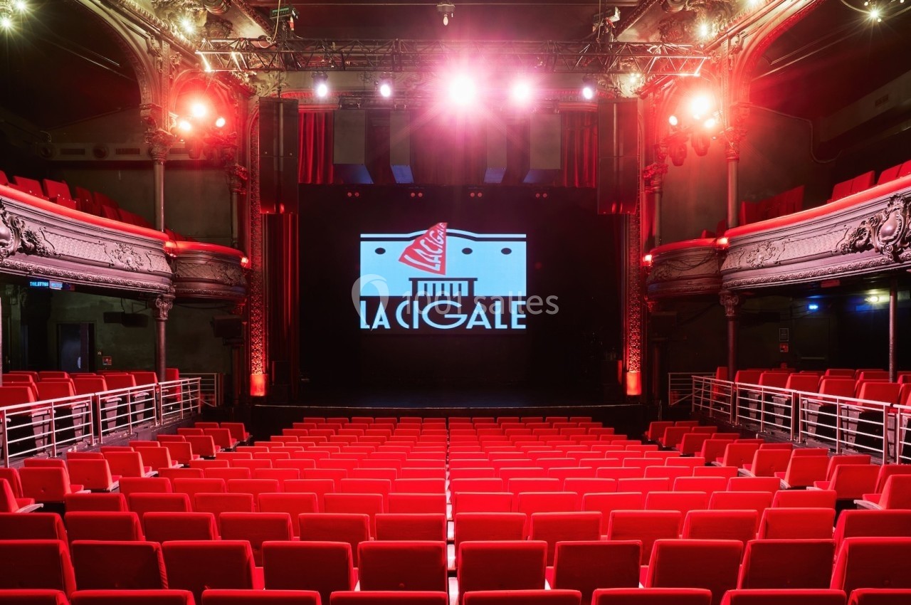 Salle de spectacle avec sièges rouges, scène éclairée et logo ’La Cigale’ projeté en arrière-plan.