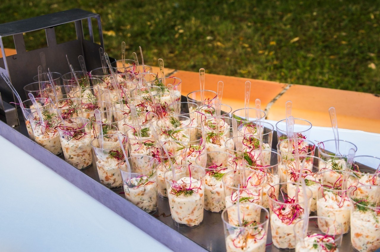 Verrines individuelles de salade garnies de fines herbes et radis, disposées sur un plateau en extérieur.