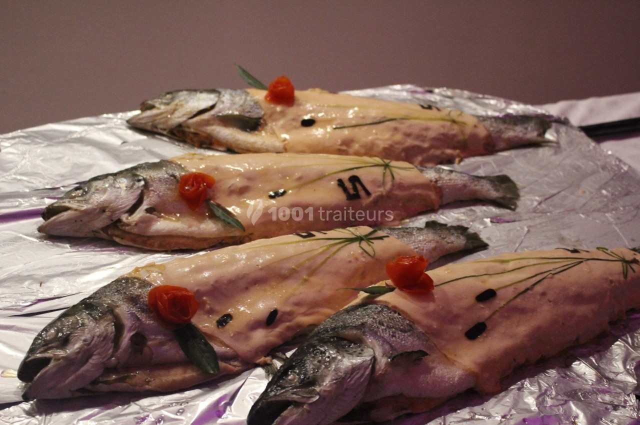 Quatre poissons entiers préparés avec une garniture crémeuse, décorés de fines herbes et de fleurs comestibles.