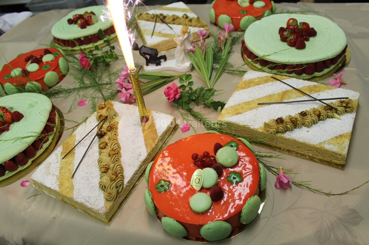 Assortiment de gâteaux décorés avec des fruits, macarons et une bougie allumée sur une table ornée de fleurs.