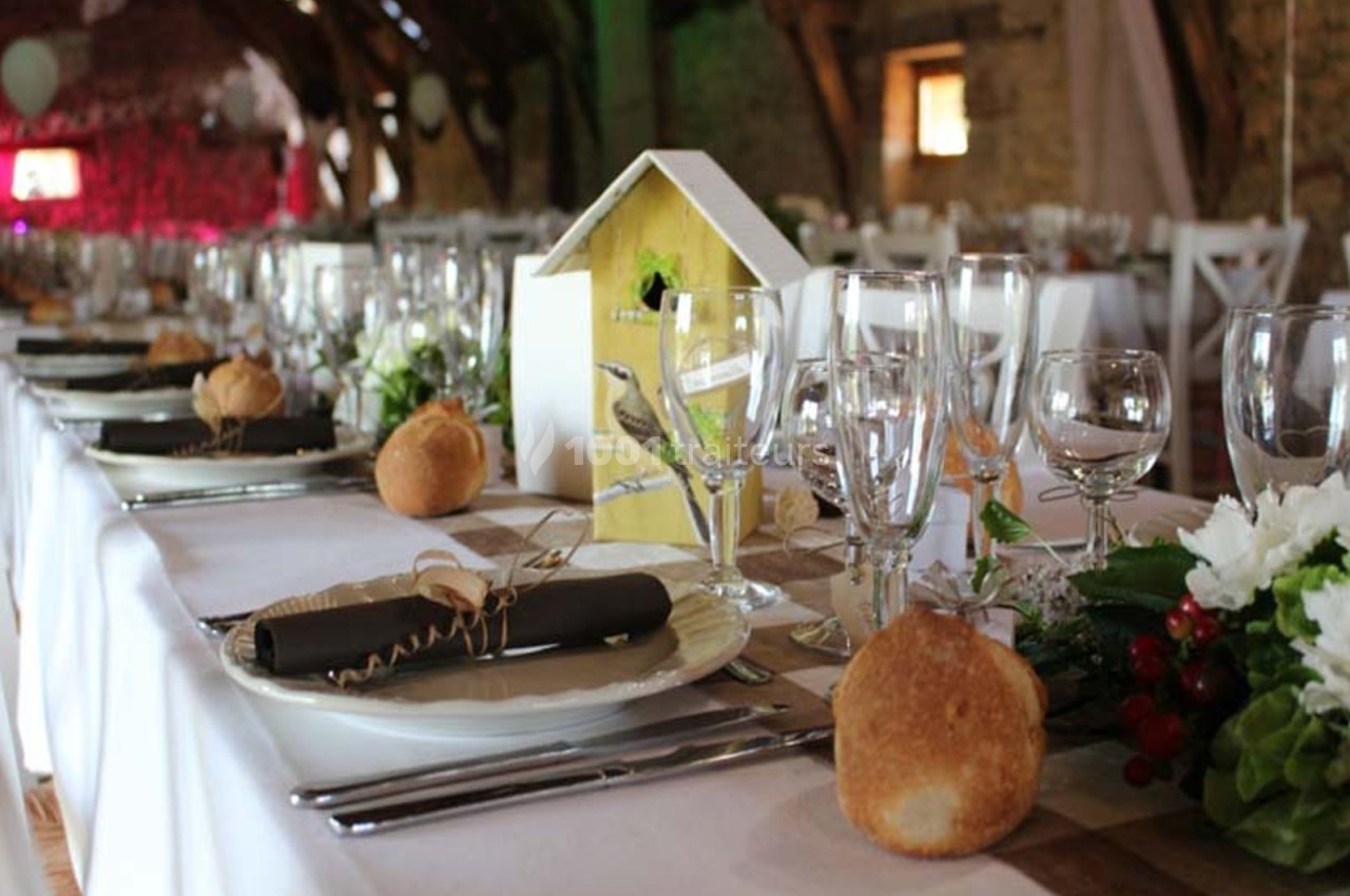 Table de réception décorée avec des assiettes, verres, serviettes noires, pains individuels et centre de table floral.