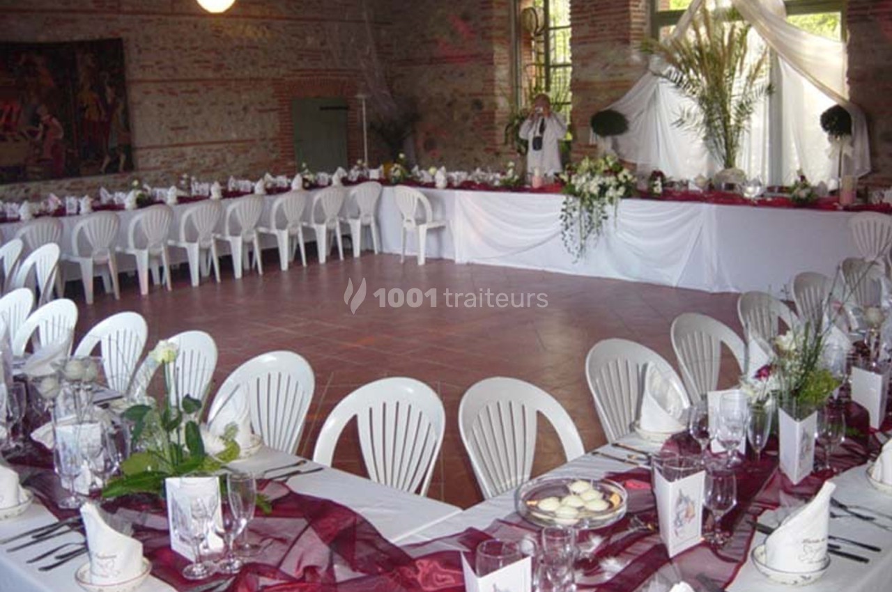 Salle de réception décorée pour un mariage, avec tables en U, nappes blanches, chaises en plastique et décor floral.