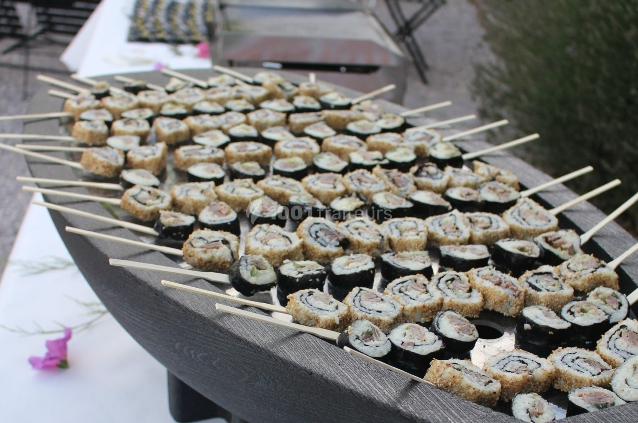 Plateau de sushis en brochettes disposés sur un support en forme de bateau, présenté en extérieur.