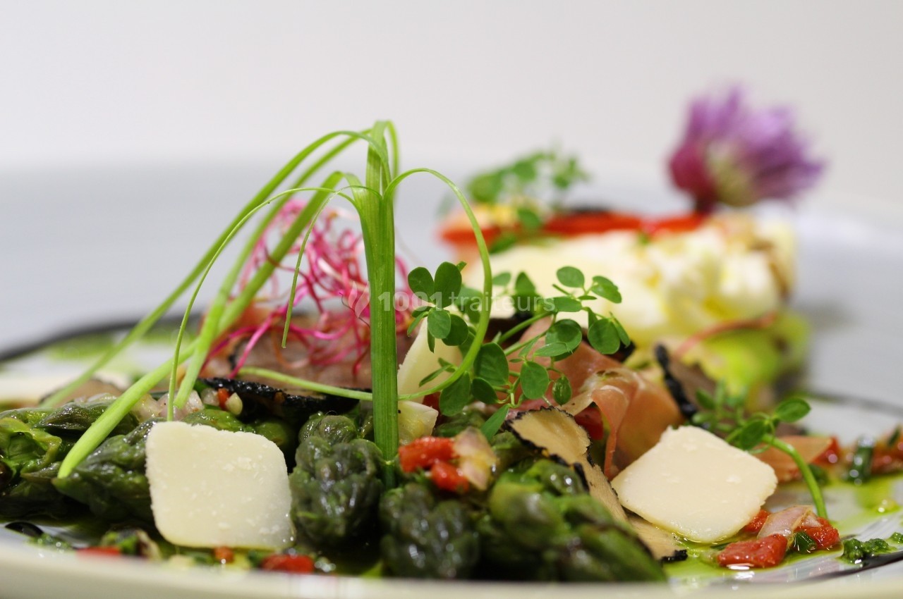 Assiette garnie d'asperges, copeaux de fromage, truffes et légumes colorés, décorée de fines herbes.