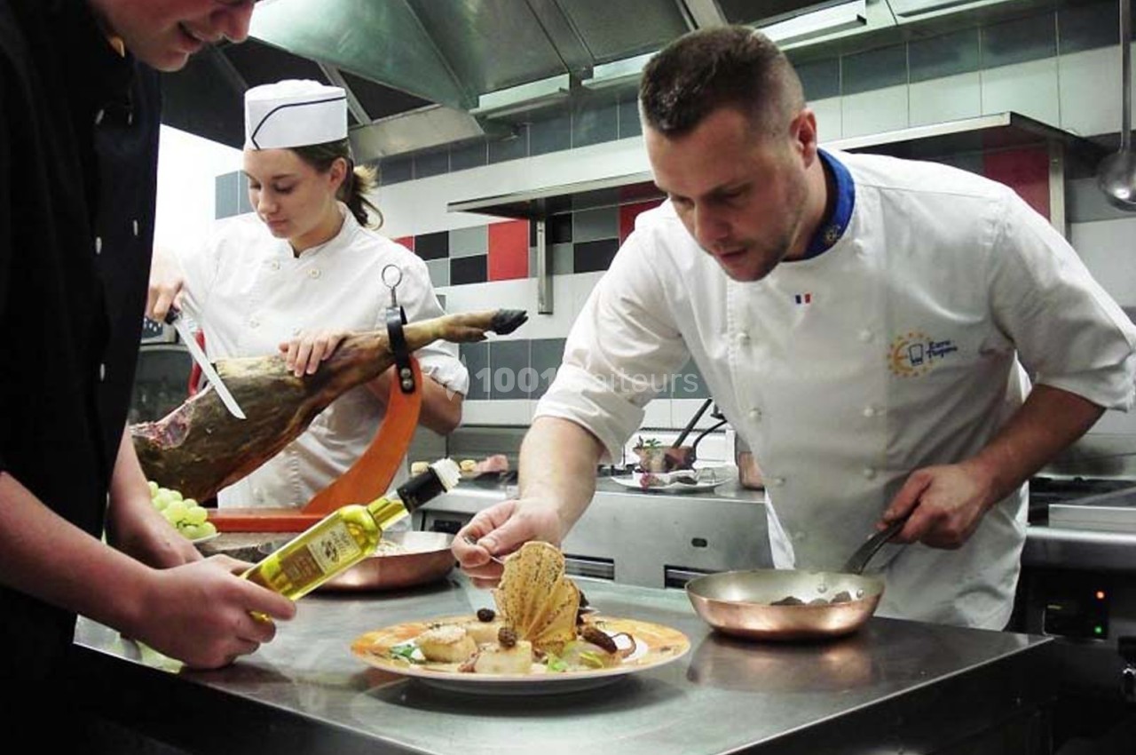 Un chef et son équipe préparent un plat dans une cuisine professionnelle avec des ingrédients frais.