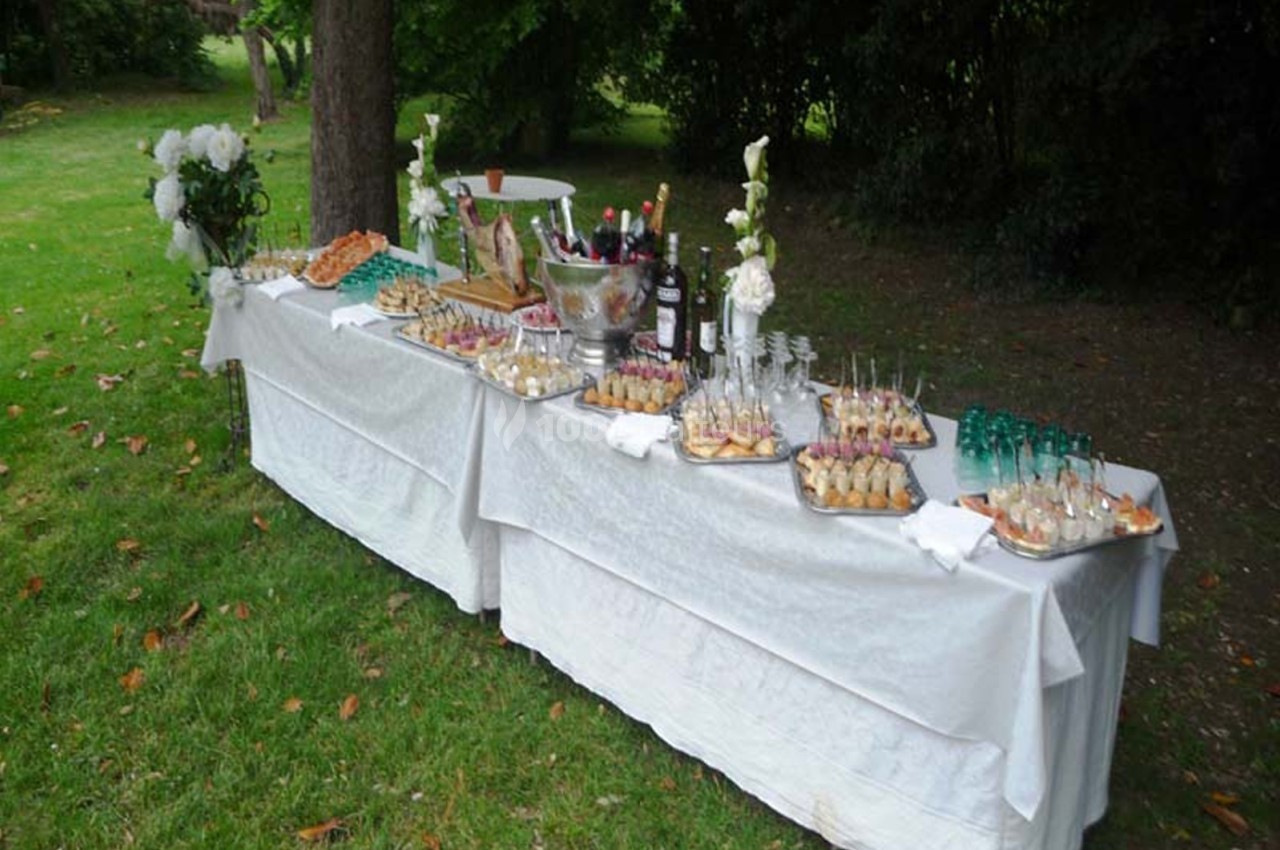 Table dressée en extérieur avec nappes blanches, proposant un buffet de boissons et amuse-bouches variés.
