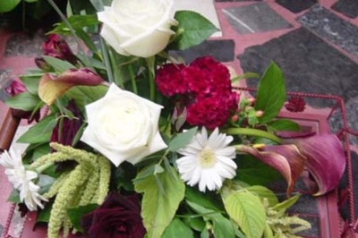 Composition florale avec roses blanches, fleurs rouges et feuillage, disposée sur un cadre rouge sur sol en mosaïque.