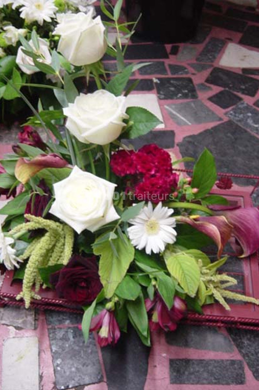 Composition florale avec roses blanches, fleurs rouges et feuillage, disposée sur un cadre rouge sur sol en mosaïque.