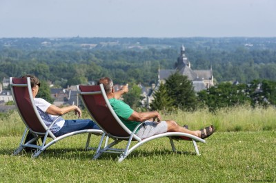 Salon lumineux avec murs en pierre, cheminée, canapé, table ronde avec chaises jaunes, et vue sur une cuisine ouverte.