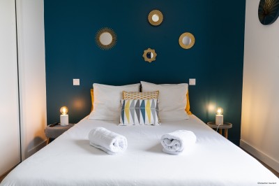 Salon lumineux avec murs en pierre, cheminée, canapé, table ronde avec chaises jaunes, et vue sur une cuisine ouverte.