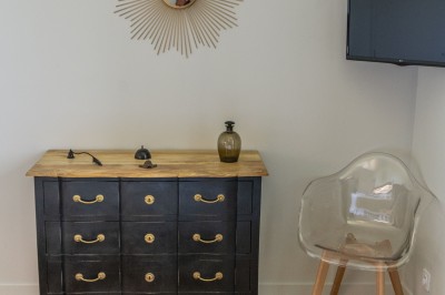 Salon lumineux avec murs en pierre, cheminée, canapé, table ronde avec chaises jaunes, et vue sur une cuisine ouverte.