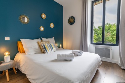 Salon lumineux avec murs en pierre, cheminée, canapé, table ronde avec chaises jaunes, et vue sur une cuisine ouverte.