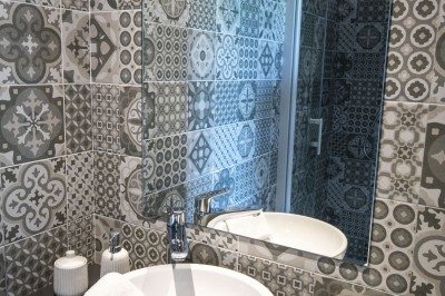 Salon lumineux avec murs en pierre, cheminée, canapé, table ronde avec chaises jaunes, et vue sur une cuisine ouverte.