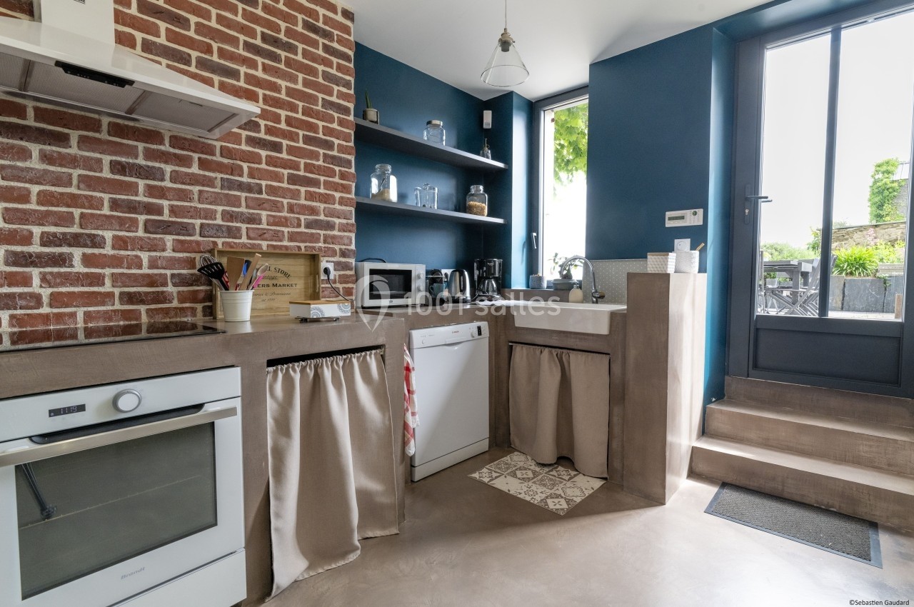 Cuisine lumineuse avec murs en briques et bleus, équipée d'un four, d'un évier, d'appareils électroménagers et d'une porte…