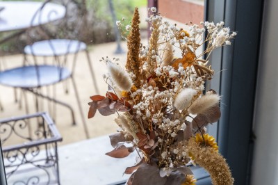 Salon lumineux avec murs en pierre, cheminée, canapé, table ronde avec chaises jaunes, et vue sur une cuisine ouverte.