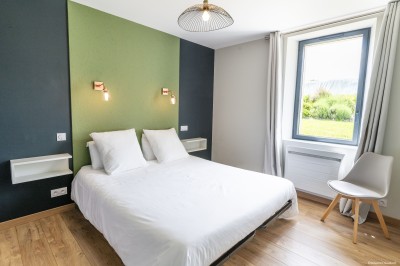 Salon lumineux avec murs en pierre, cheminée, canapé, table ronde avec chaises jaunes, et vue sur une cuisine ouverte.