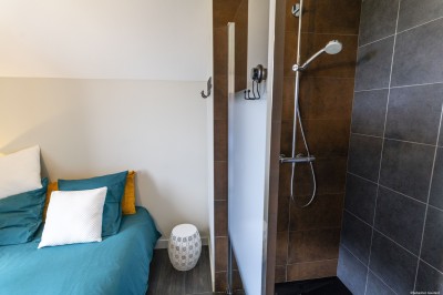 Salon lumineux avec murs en pierre, cheminée, canapé, table ronde avec chaises jaunes, et vue sur une cuisine ouverte.