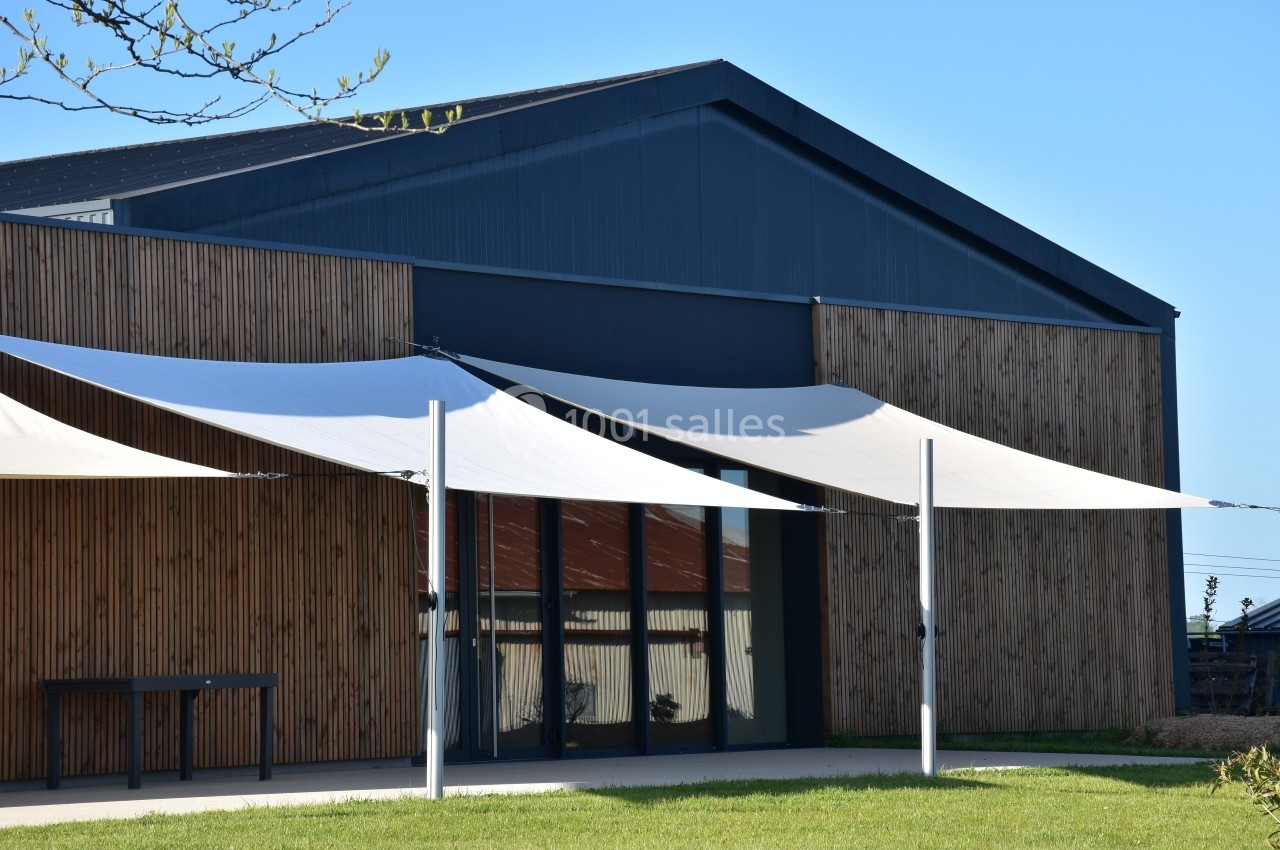 Bâtiment moderne en bois avec des voiles d'ombrage blanches tendues devant une façade vitrée.