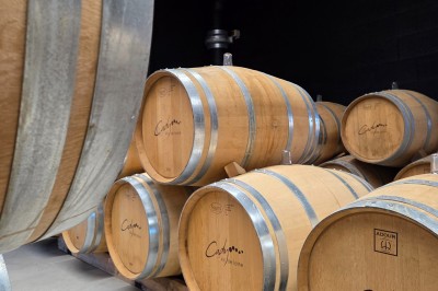 Salon lumineux avec murs en pierre, cheminée, canapé, table ronde avec chaises jaunes et vue sur une cuisine ouverte.