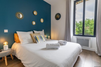 Salon lumineux avec murs en pierre, cheminée, canapé, table ronde avec chaises jaunes et vue sur une cuisine ouverte.