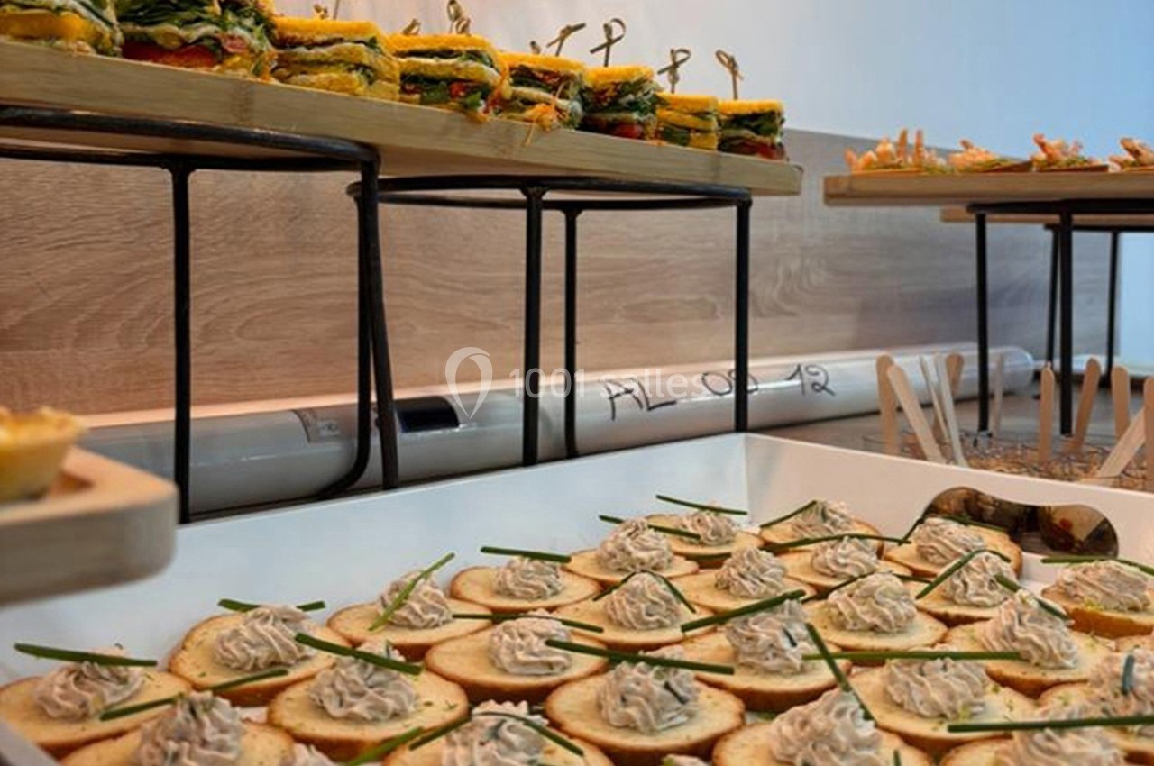 Plateau de canapés garnis de crème et ciboulette, avec en arrière-plan des sandwichs et amuse-bouches variés.