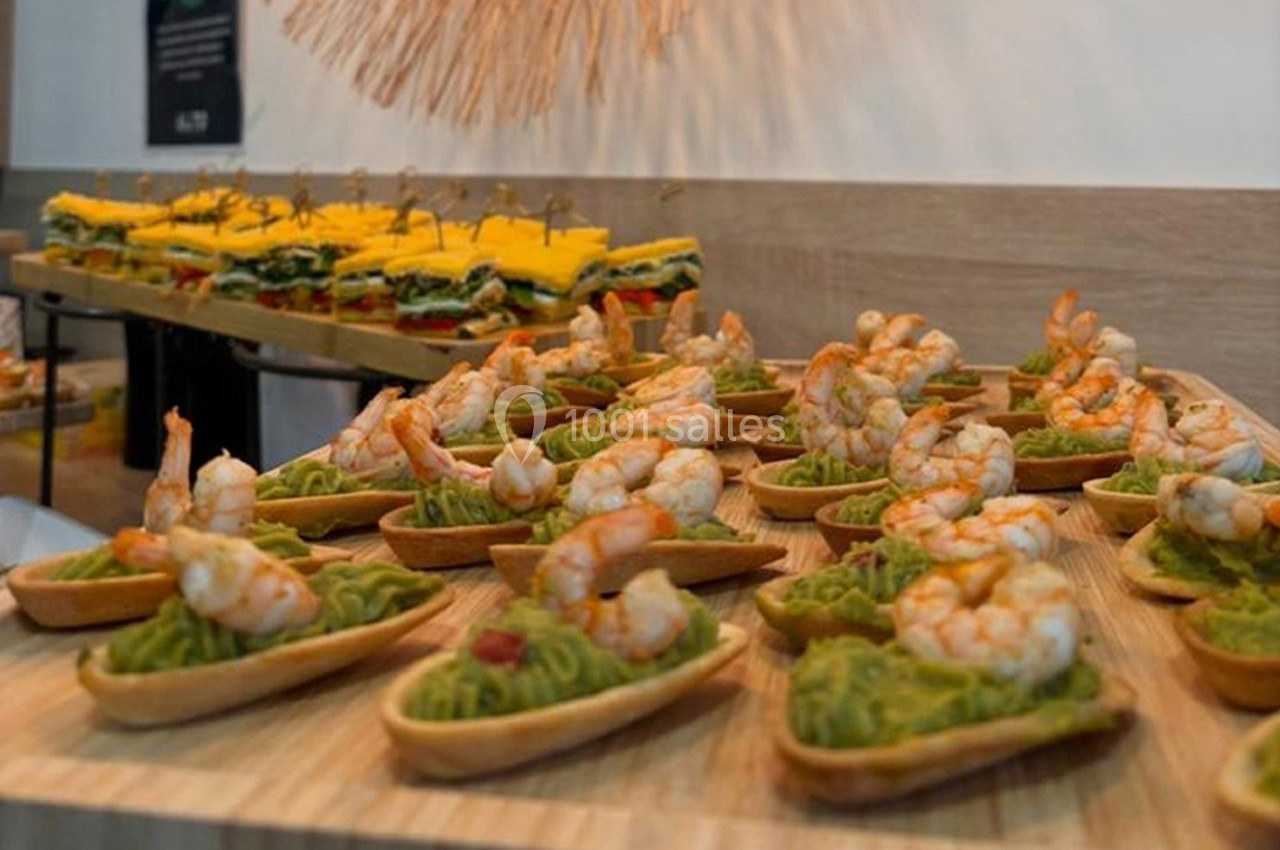 Plateau de bouchées apéritives avec des crevettes sur lit de guacamole, disposées sur une table en bois.