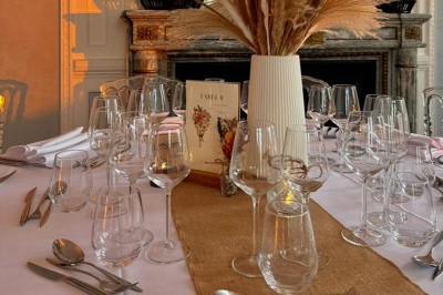 Table ronde dressée pour un repas, avec nappes blanches, couverts, verres, pains et centre de table floral.