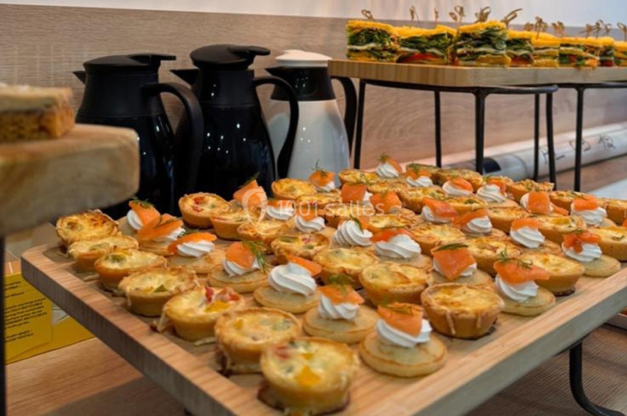 Plateau de bouchées salées variées avec quiches, saumon fumé et verrines, accompagné de carafes en arrière-plan.