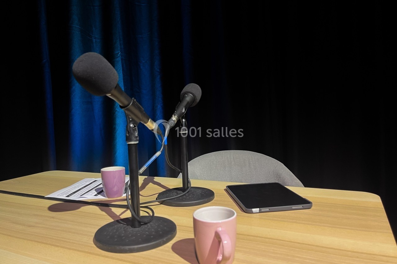 Deux microphones sur une table en bois avec des tasses, une tablette et des documents, devant un fond sombre.