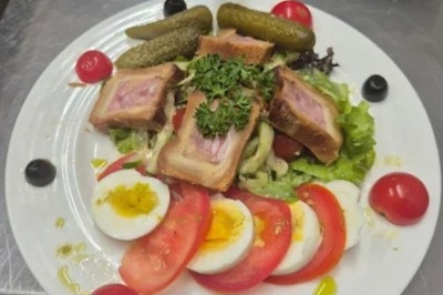 Assiette de salade composée avec feuilles de laitue, tomates, carottes, noix et un morceau de fromage grillé.