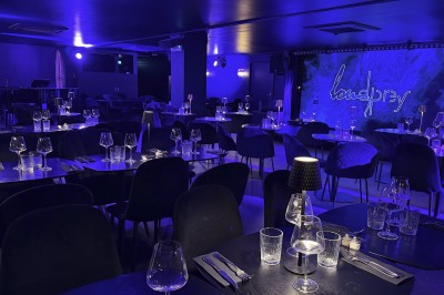 Salle de restaurant élégante avec tables dressées, éclairage tamisé bleu et petites lampes sur chaque table.