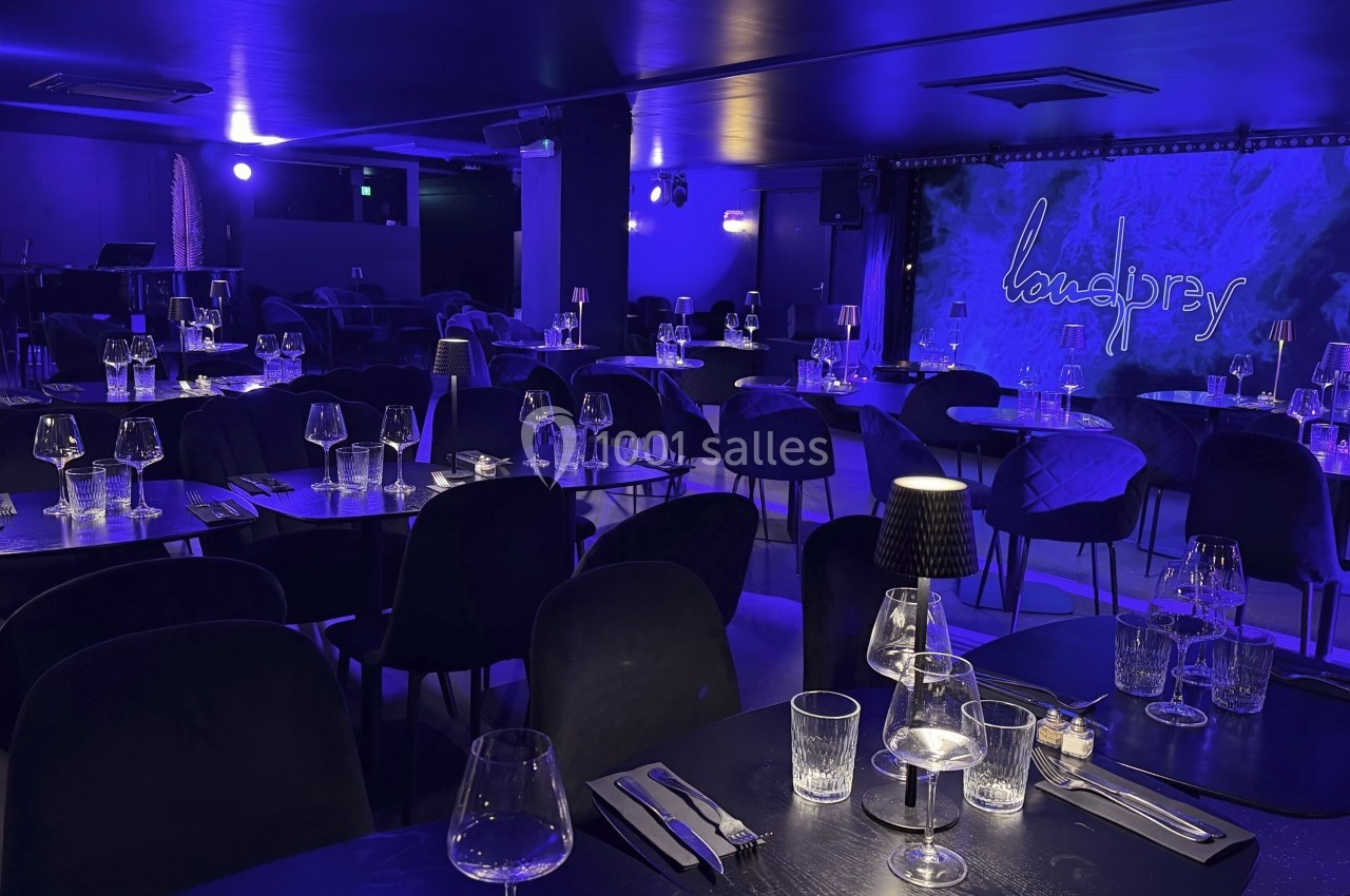 Salle de spectacle intimiste avec tables dressées, éclairage tamisé et scène en arrière-plan.