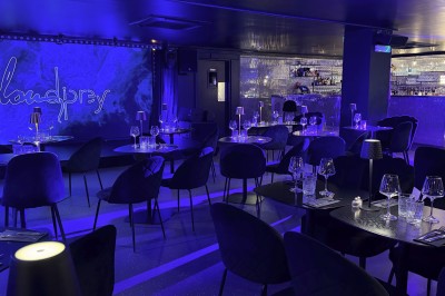 Salle de restaurant élégante avec tables dressées, éclairage tamisé bleu et petites lampes sur chaque table.
