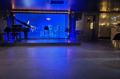 Miniature Location salle Paris 10 (Paris) - Lou Diprey #2 Salle de spectacle avec scène éclairée en bleu, équipée d'un piano, de micros et de chaises devant des tables.