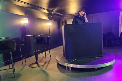 Miniature Location salle Paris 10 (Paris) - Lou Diprey #12 Salle de spectacle avec scène éclairée en bleu, équipée d'un piano, de micros et de chaises devant des tables.