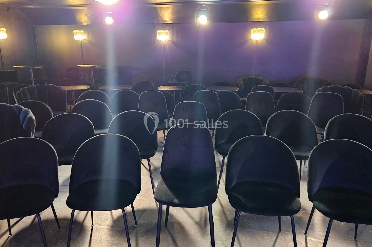 Salle vide avec des rangées de chaises noires alignées sous un éclairage tamisé.