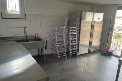 Cuisine professionnelle avec plan de travail en inox, carrelage mural blanc, sol en carrelage gris et équipements basiques.