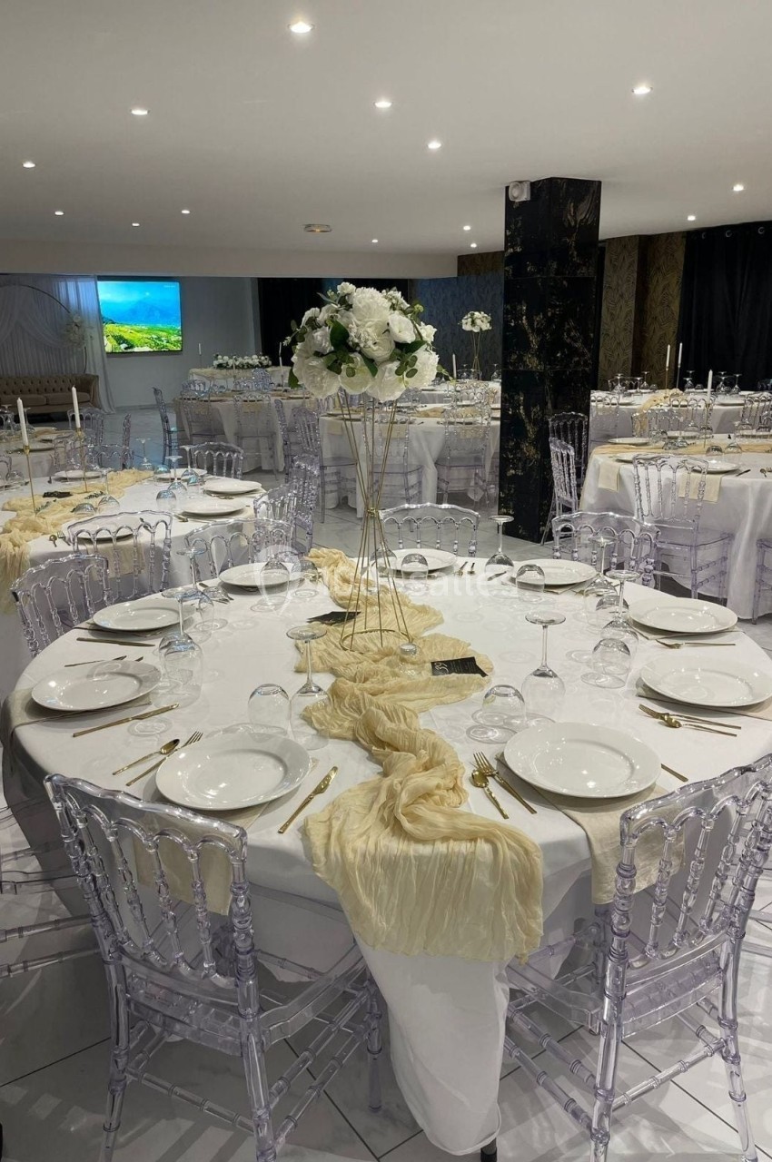Salle de réception élégamment décorée avec des tables rondes, nappes blanches, chaises transparentes et centres de table…