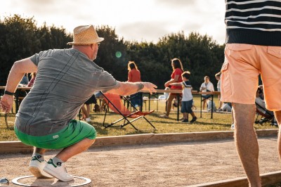 Miniature Location salle Coquelles (Pas-de-Calais) - The Place To Bee #15 Un homme lance une boule de pétanque sur un terrain en plein air, entouré de spectateurs et de joueurs.