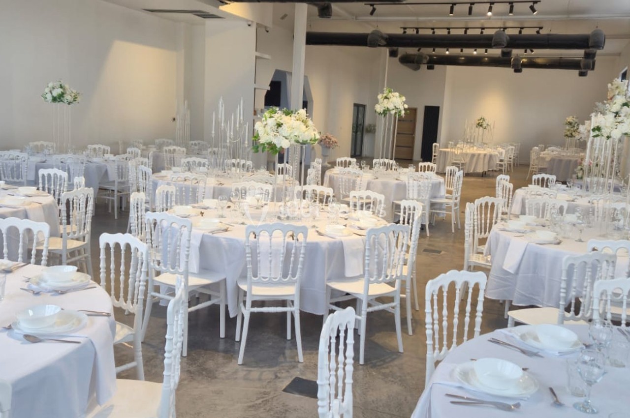 Salle de réception lumineuse avec des tables rondes dressées, décorées de nappes blanches et de centres de table fleuris.