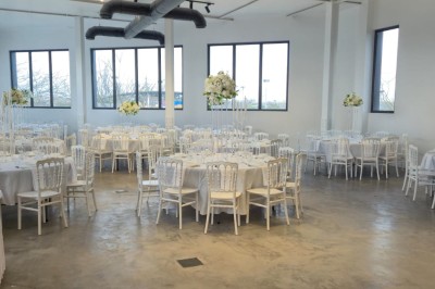 Miniature Location salle Épinay-sur-Seine (Seine-Saint-Denis) - Salle Delena #12 Salle lumineuse avec table ronde dressée, chaises blanches et centre de table floral sous de grandes fenêtres.